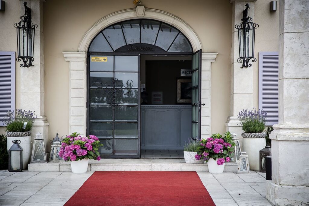 duże szklane drzwi, czerwony dywan i kwiaty przed wejściem